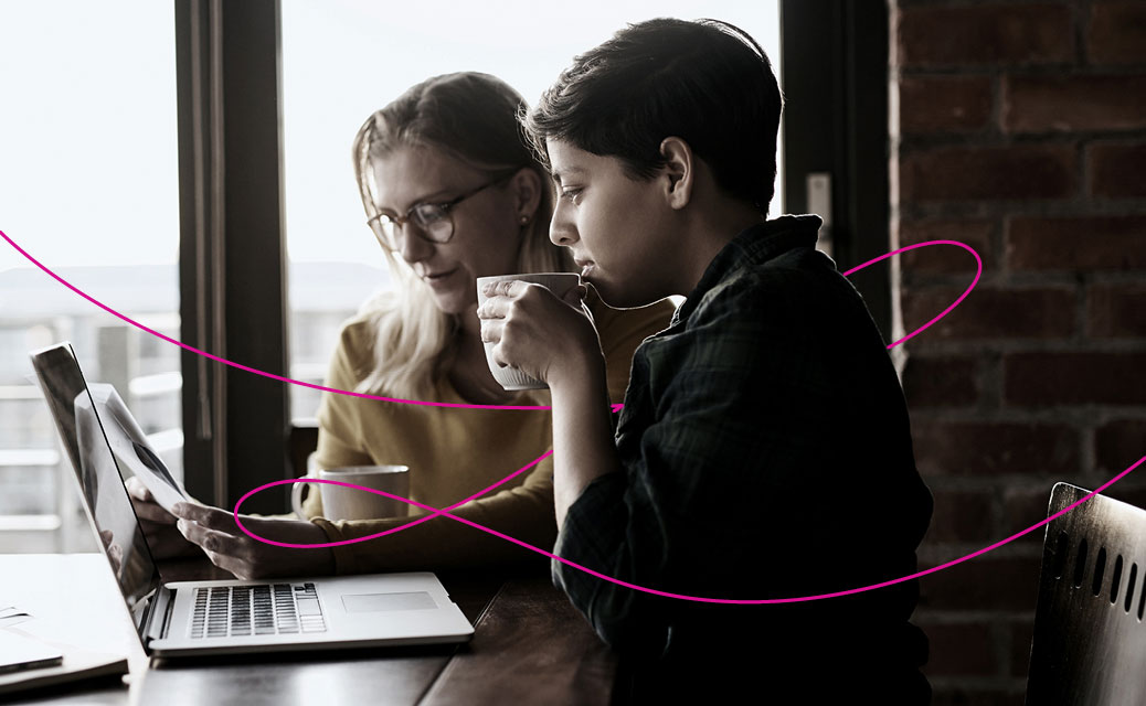 Two young women sitting at a table in front of paperwork and a laptop